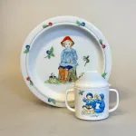 Elsa Beskow Flad Tallerken - Putte i Blåbærskoven, Elsa Beskow Krus med Låg - Putte i blåbærskoven, blomsterfesten, blomsternes bog, astrid lindgren, billedbøger, eventyr, illustrationer, tegninger, tudkop, kop, krus, lågkrus, baby, babyshower, barnedåb, dåbsgave, barselsgave, svensk, nostalgisk, service, til børn, drikke, tud, biti, ribe